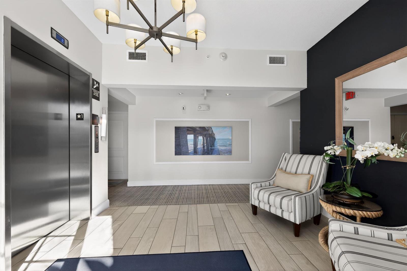 A modern elevator lobby features a striped armchair, a chandelier, and a framed pier painting — 915 Bay Colony Drive S, Juno Beach FL 33408, JUNO BEACH, FL