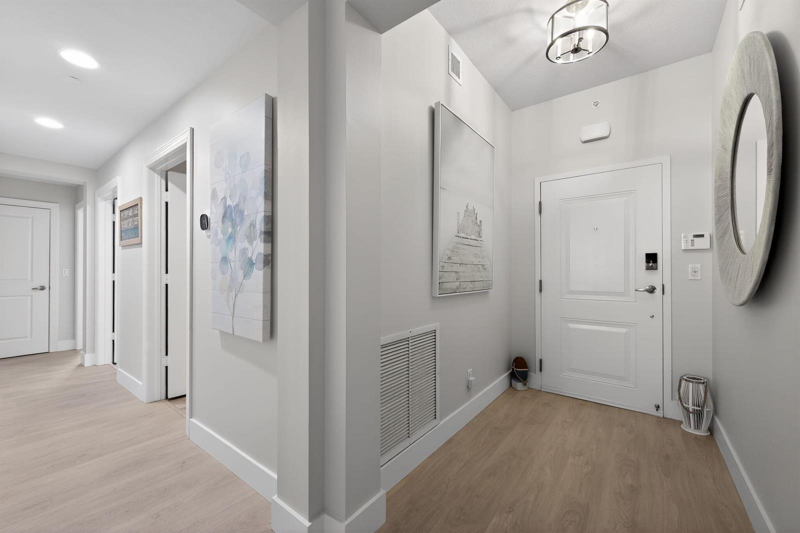 A bright entryway features light wood flooring, white walls, a front door, and wall art — 915 Bay Colony Drive S, Juno Beach FL 33408, JUNO BEACH, FL
