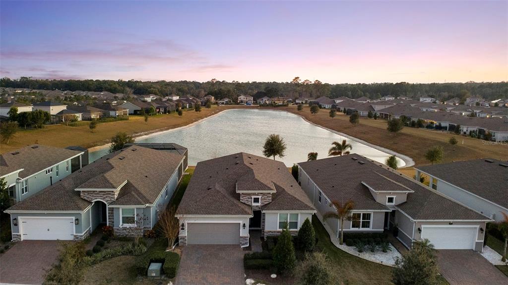 An aerial view shows three suburban houses with brown roofs situated along a pond — 1188 VICTORIA HILLS DRIVE N, DELAND, FL