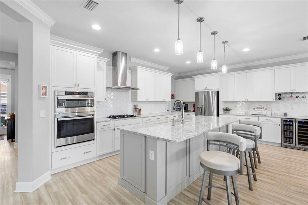 A modern kitchen features white cabinetry, a gray island with bar stools, and stainless appliances — 1188 VICTORIA HILLS DRIVE N, DELAND, FL