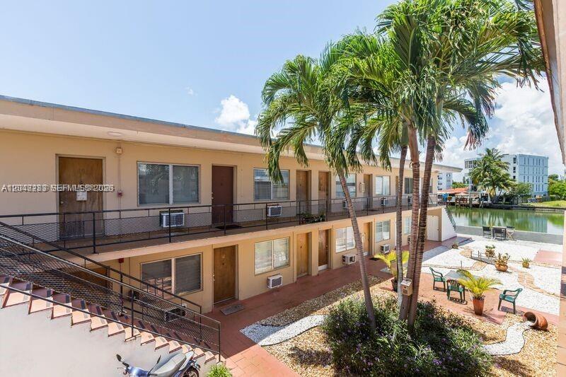 An exterior view of a two-story apartment building with palm trees and a canal — 8210 Byron Ave # 16, Miami Beach FL 33141, MIAMI BEACH, FL