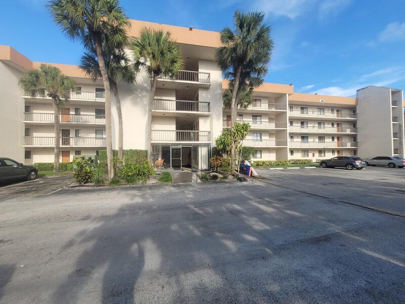 A three-story apartment building with a central entrance, balconies, and palm trees in the foreground — 5917 Via Vermilya # 206, Lake Worth FL 33462, LAKE WORTH, FL