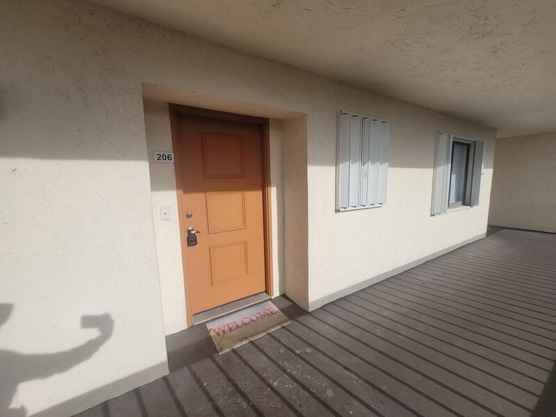 An exterior view of an apartment door numbered 206 with a welcome mat on a balcony — 5917 Via Vermilya # 206, Lake Worth FL 33462, LAKE WORTH, FL