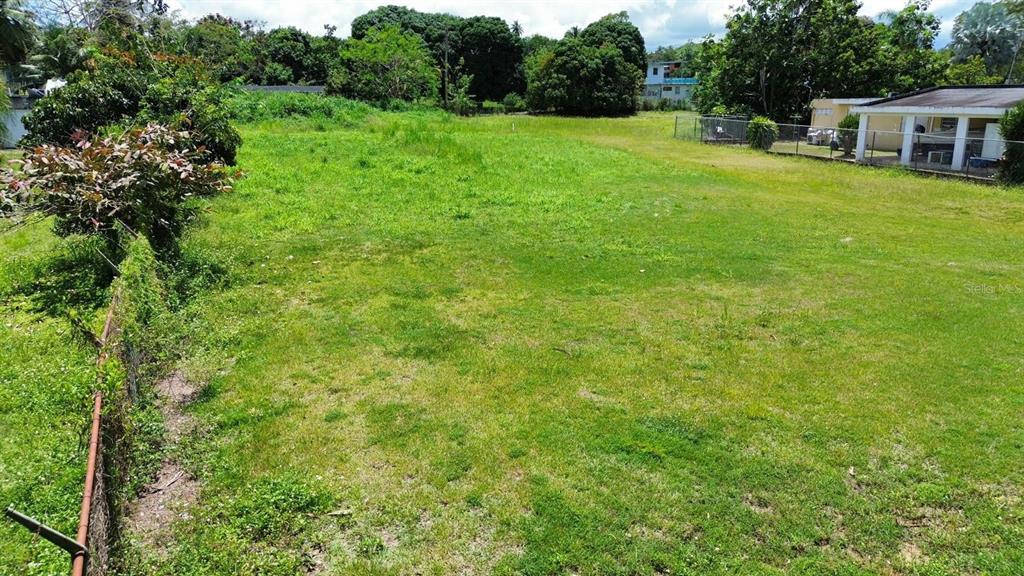 A grassy, vacant lot is enclosed by a chain-link fence next to a residential building — BO COTO NORTE, SECTOR GUAYANEY, MANATI, MANATI, PR