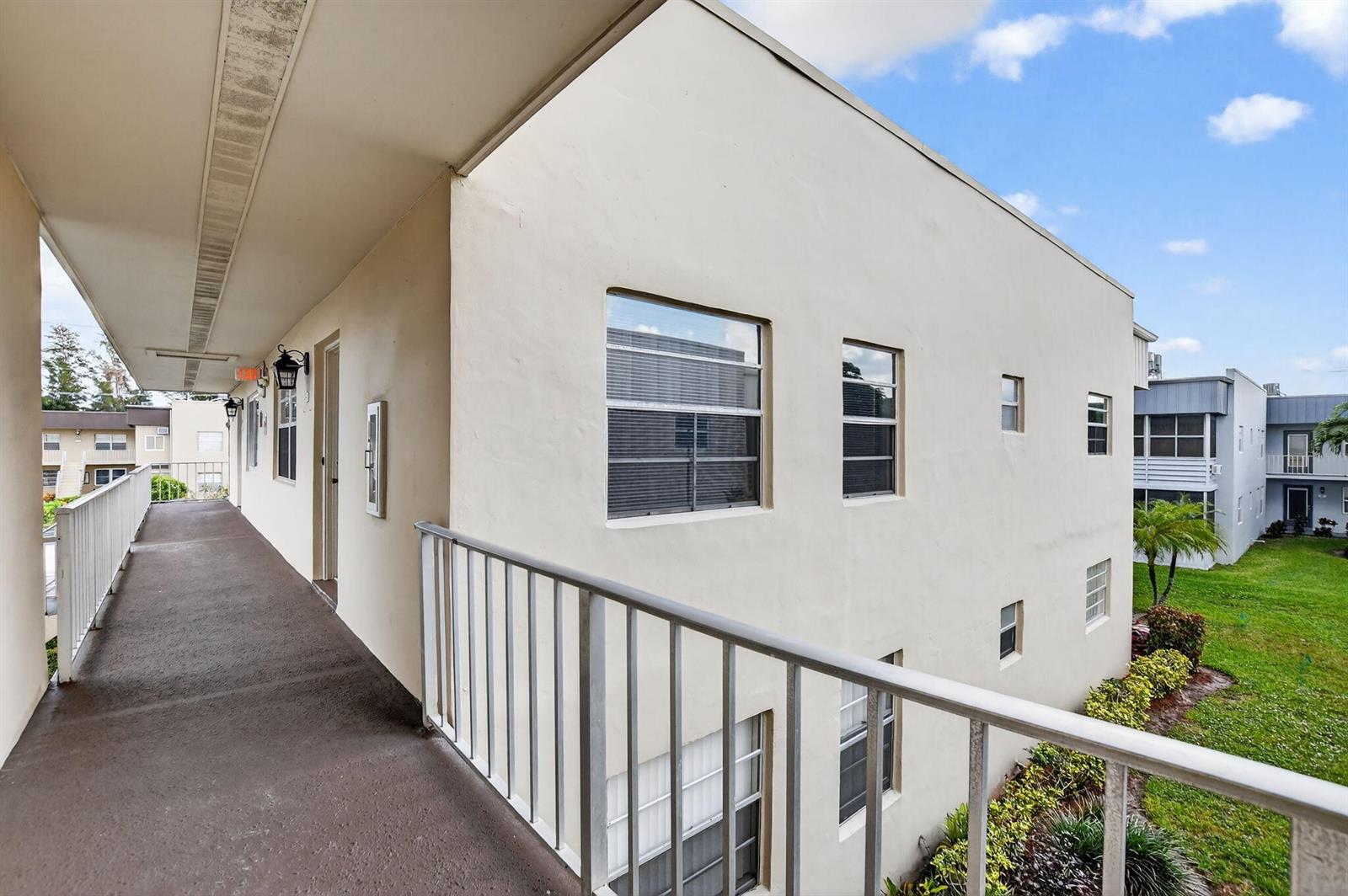 An exterior view of an apartment building balcony with a metal railing and beige walls — 74 Burgundy B, Delray Beach FL 33484, DELRAY BEACH, FL