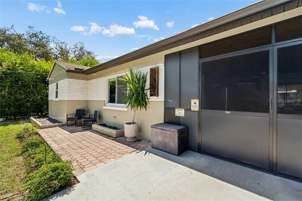 A paved patio sits beside a house exterior with a screened-in porch and landscaping — 1904 W MEADOWBROOK AVENUE, TAMPA, FL