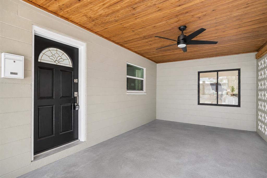 A covered porch with a black front door, ceiling fan, and light-colored block walls — 1904 W MEADOWBROOK AVENUE, TAMPA, FL