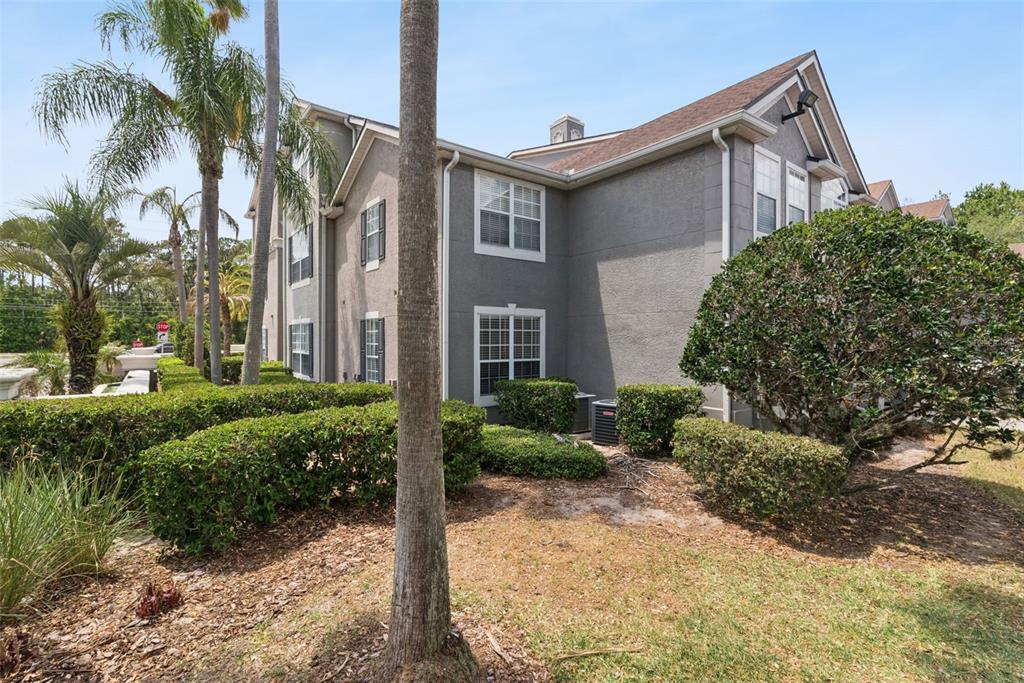 A multi-story gray stucco apartment building is surrounded by palm trees and manicured hedges — 3307 S KIRKMAN ROAD UNIT 110, ORLANDO, FL