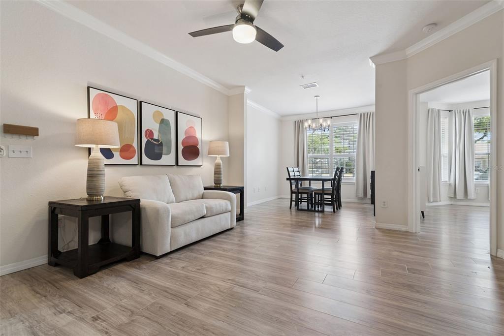 A living room with light wood flooring, a beige sofa, and an adjacent dining area — 3307 S KIRKMAN ROAD UNIT 110, ORLANDO, FL