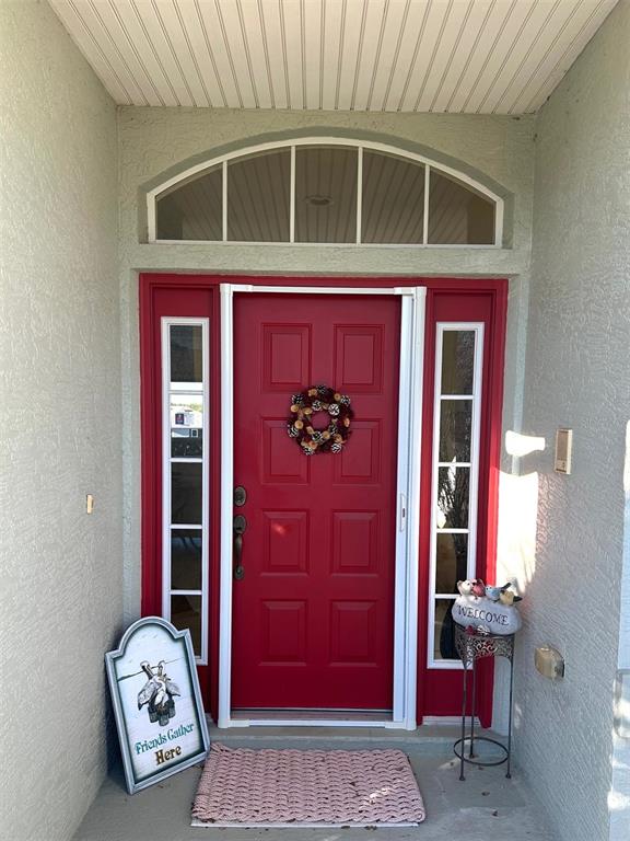 A red front door with sidelights and a transom window sits under a covered porch — 251 W REXFORD DRIVE, BEVERLY HILLS, FL