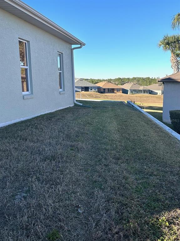 A view of a grassy side yard next to a light-colored house with two windows — 251 W REXFORD DRIVE, BEVERLY HILLS, FL