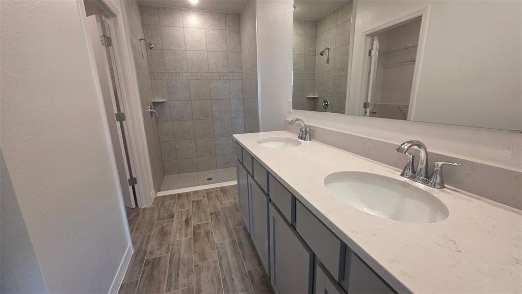 A bathroom features a double vanity with light countertops, gray cabinets, and a tiled shower — 5535 MADDIE DRIVE, HAINES CITY, FL