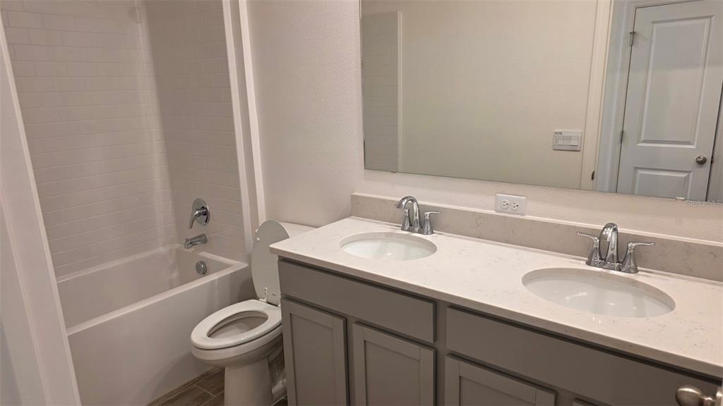 A bathroom features a double vanity with light countertops, gray cabinets, and a shower-tub combo — 5535 MADDIE DRIVE, HAINES CITY, FL