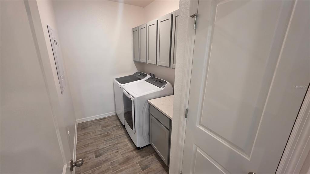 A laundry room features grey cabinets, white appliances, and wood-look tile flooring — 5535 MADDIE DRIVE, HAINES CITY, FL