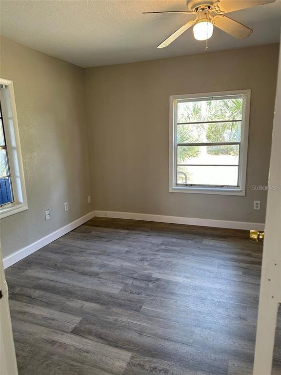 An empty bedroom features gray wood-look flooring, light-colored walls, a ceiling fan, and two windows — 1219 W 8TH STREET, SANFORD, FL