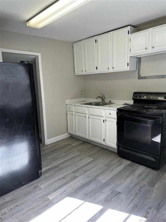 A kitchen features white cabinets, a black stove, a black refrigerator, and gray wood-look flooring — 1219 W 8TH STREET, SANFORD, FL