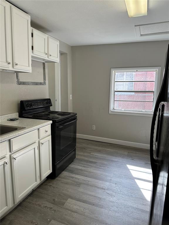 A kitchen features white cabinets, a black stove, and light wood-look flooring — 1219 W 8TH STREET, SANFORD, FL