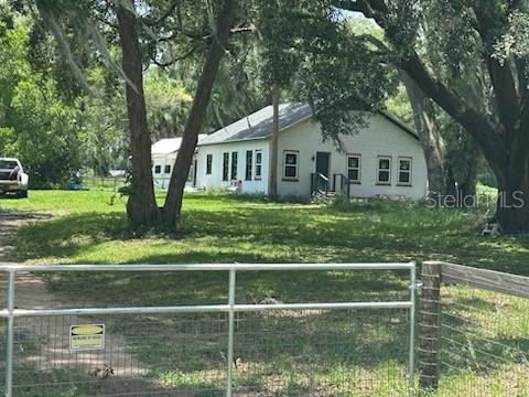 A white, single-story house sits on a grassy lot behind a metal fence — 14854 NE JACKSONVILLE ROAD, CITRA, FL