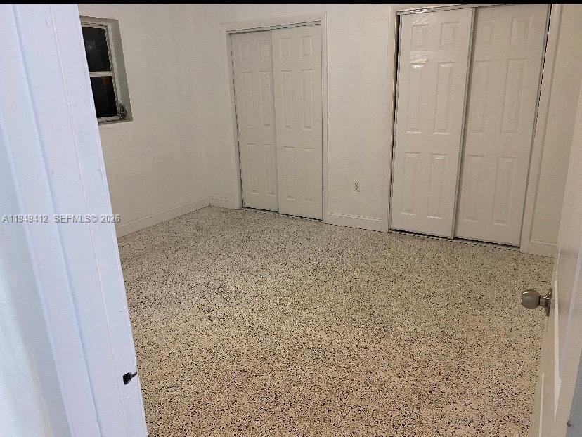 A bedroom features white walls, a speckled floor, and two sets of white closet doors — 626 NE 61st St # 5, Miami FL 33137, MIAMI, FL