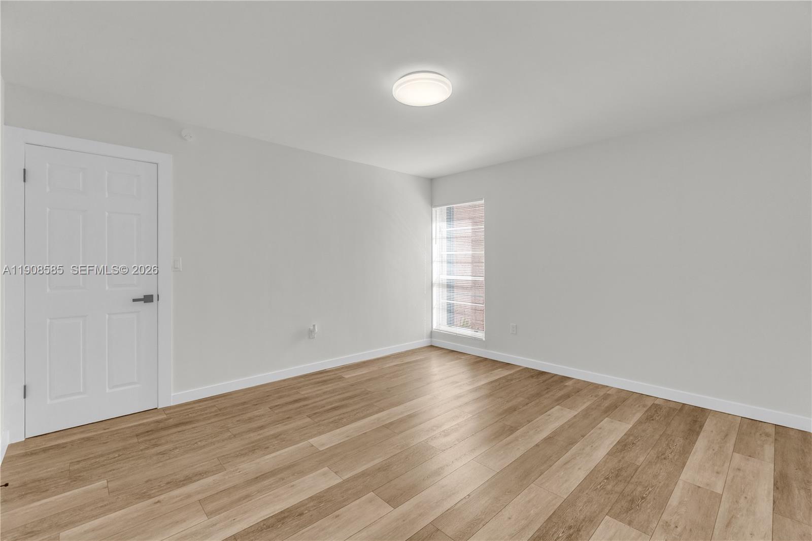 An empty room features light gray walls, wood-look flooring, a white door, and a window — 4709 NW 7th St # 9, Miami FL 33126, MIAMI, FL