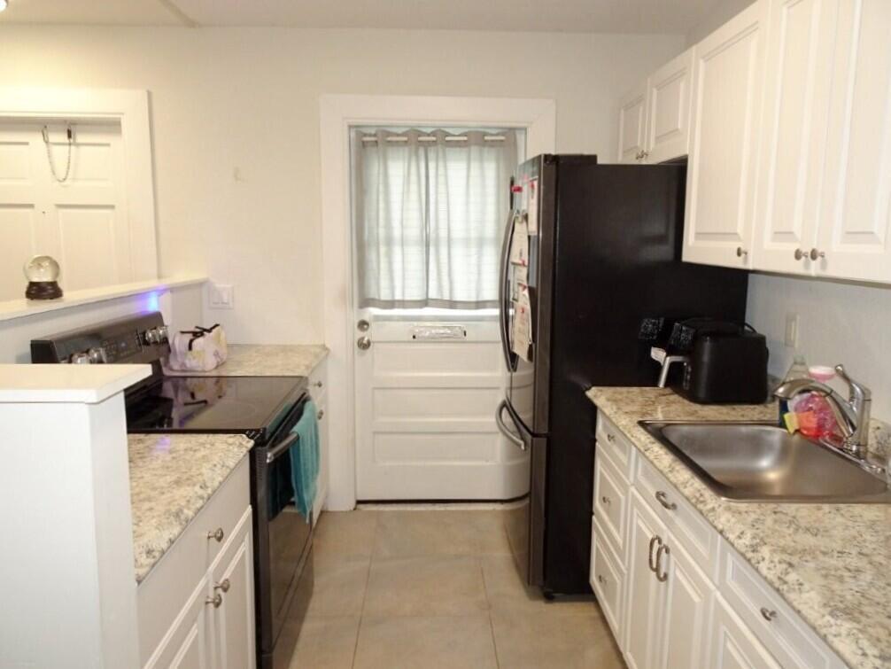 A kitchen with white cabinets, granite countertops, a black refrigerator, and a stainless steel sink — 213 SE 3rd Avenue # 2a, Boynton Beach FL 33435, BOYNTON BEACH, FL