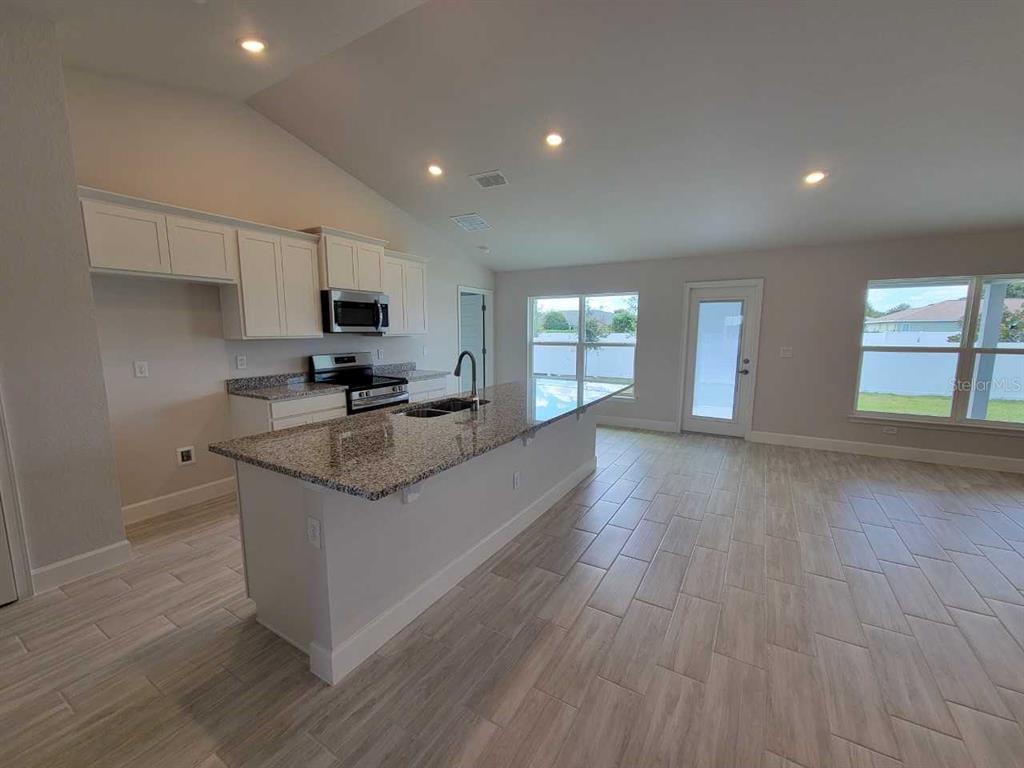 A modern kitchen features white cabinets, granite countertops, a central island, and light tile flooring — 14578 SW 69TH COURT ROAD, OCALA, FL