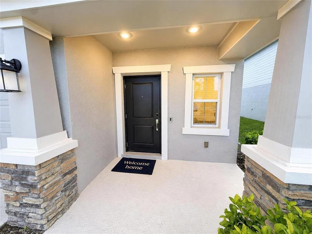 A covered front porch features a black door, a welcome mat, and stone-accented columns — 1181 SAND TRAP COURT, DAYTONA BEACH, FL