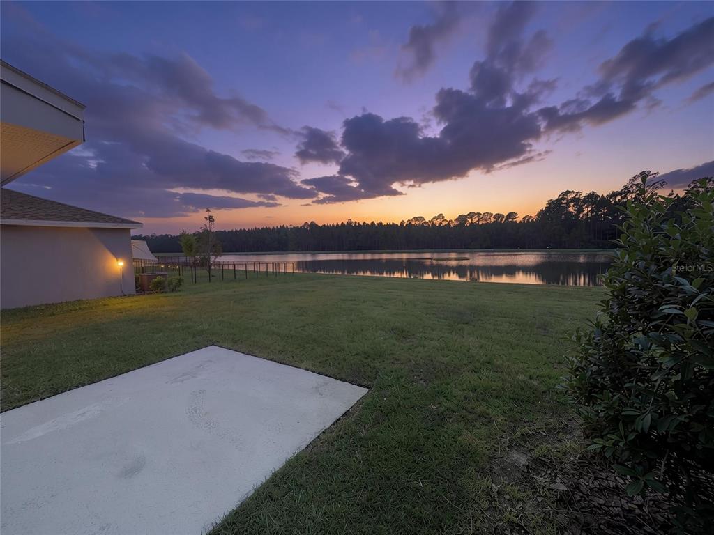 A backyard view of a lake at sunset with a concrete patio and house corner — 1181 SAND TRAP COURT, DAYTONA BEACH, FL