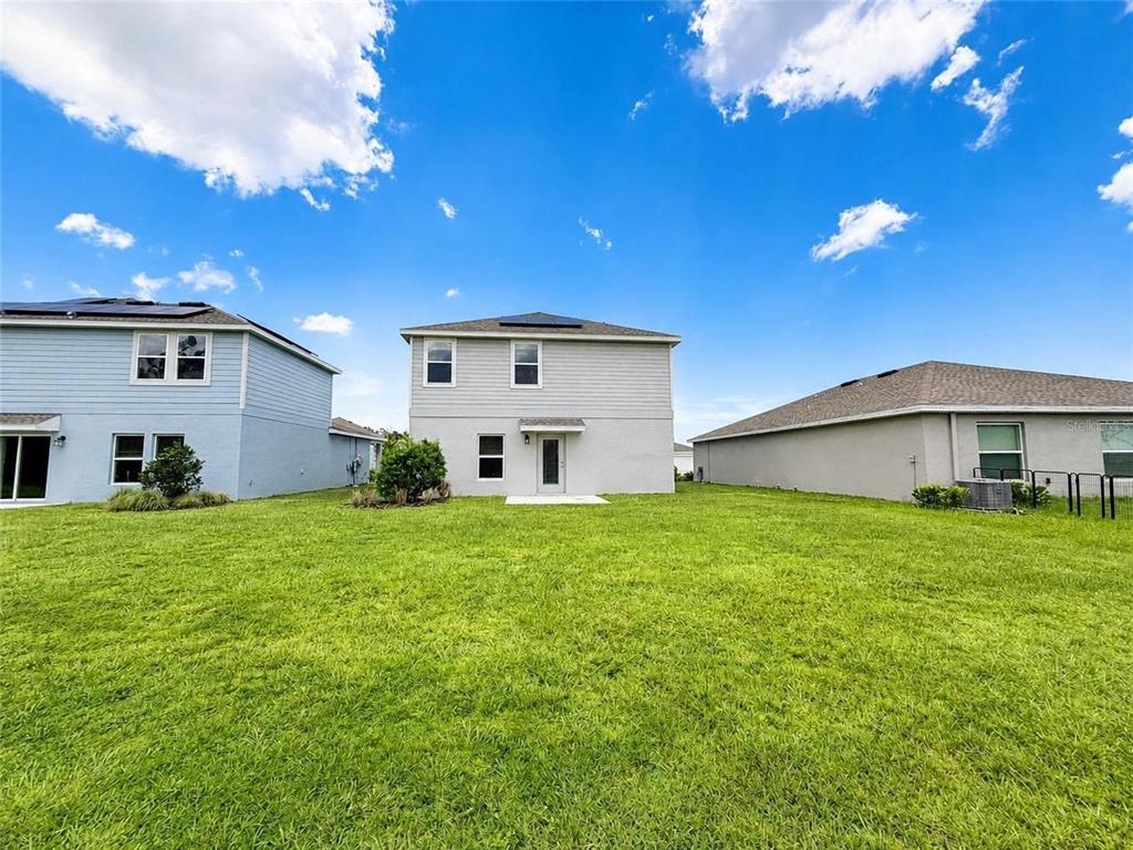 The rear exterior of a two-story light gray house with a large grassy backyard — 1181 SAND TRAP COURT, DAYTONA BEACH, FL