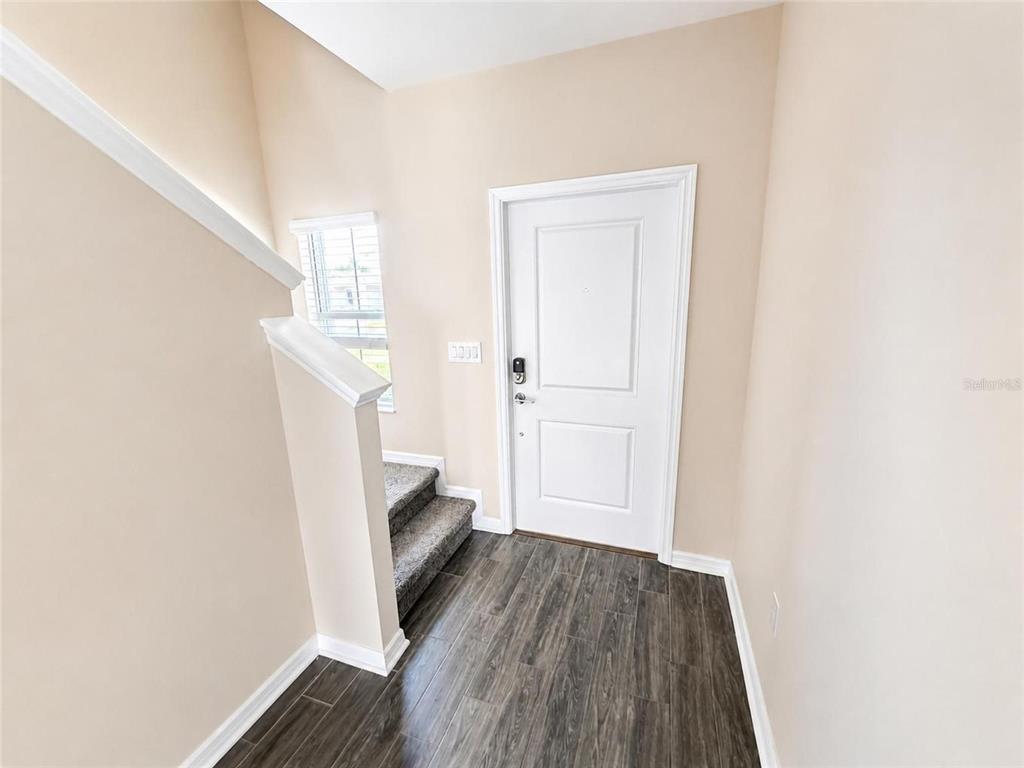 An entryway features wood-look flooring, a white front door, and stairs with carpeted steps — 1181 SAND TRAP COURT, DAYTONA BEACH, FL