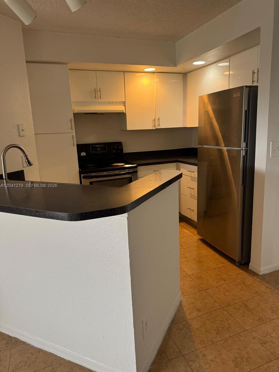 A kitchen features white cabinets, stainless steel appliances, and a black countertop peninsula — 3400 N Pinewalk Dr N # 924, Margate FL 33063, MARGATE, FL