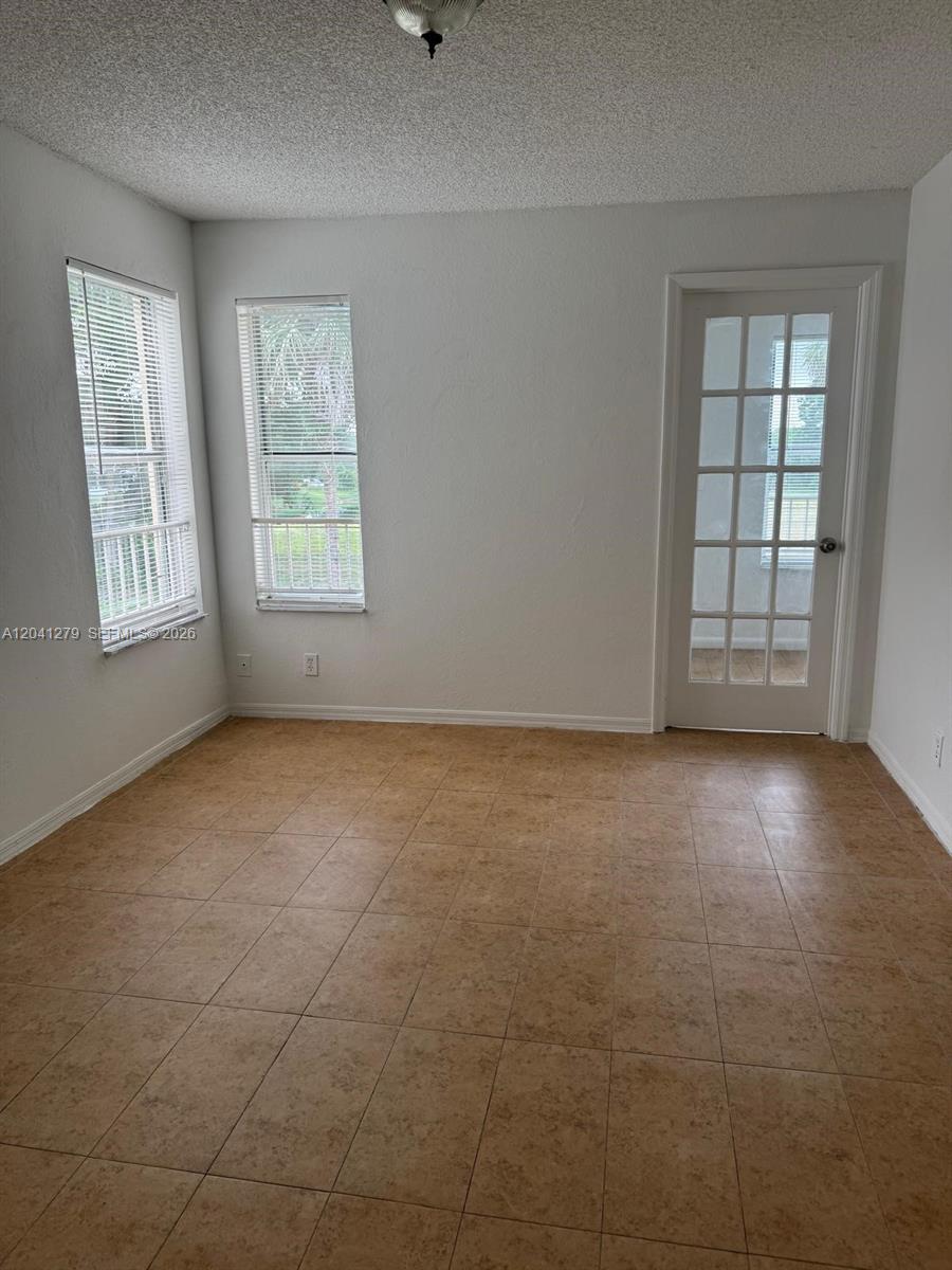 An empty room features tan tile flooring, two windows with blinds, and a glass-paneled door — 3400 N Pinewalk Dr N # 924, Margate FL 33063, MARGATE, FL