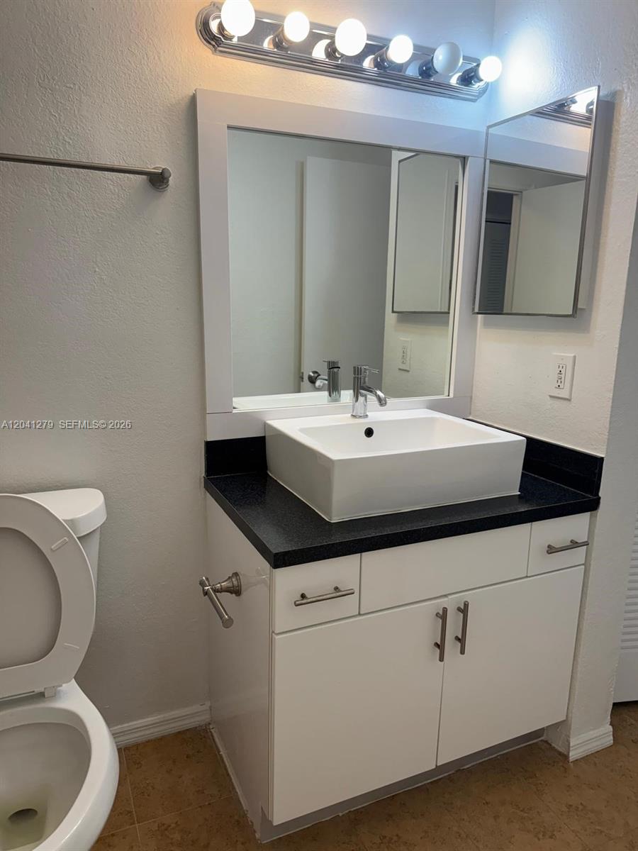 A bathroom features a white vessel sink on a black countertop above white cabinets — 3400 N Pinewalk Dr N # 924, Margate FL 33063, MARGATE, FL