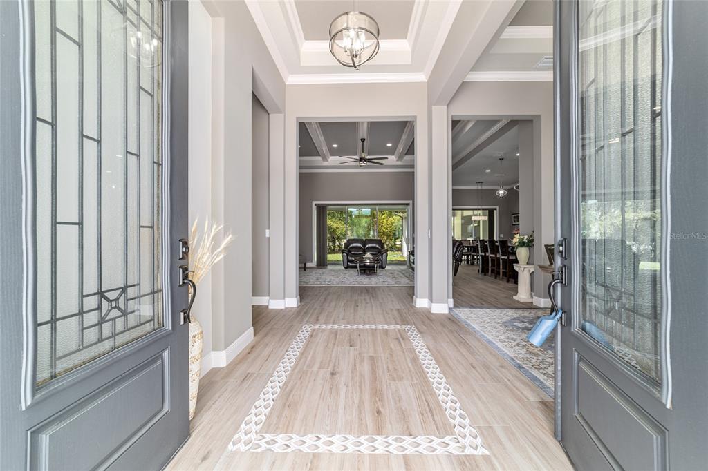An entryway with light wood-look tile flooring leads to a living area with tray ceilings — 1003 SE 46TH STREET, OCALA, FL
