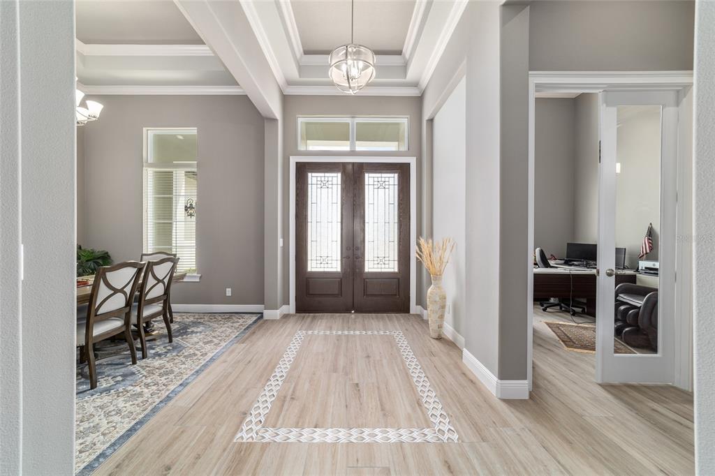 A foyer with wood-look tile flooring, a tray ceiling, double front doors, and a dining area — 1003 SE 46TH STREET, OCALA, FL
