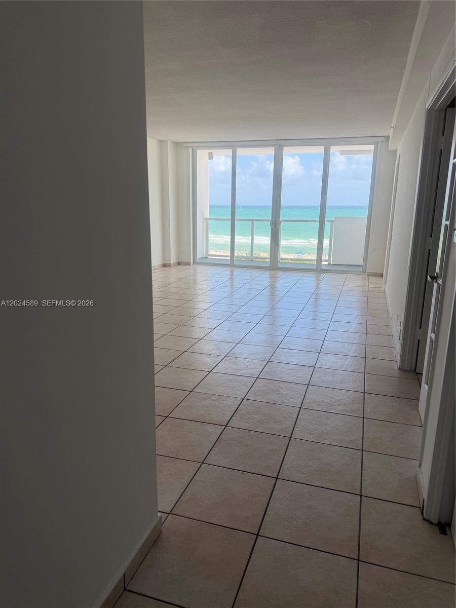 An empty room with light-colored tile flooring features a large glass wall overlooking the ocean — 5601 COLLINS AV # 607, Miami Beach FL 33140, MIAMI BEACH, FL