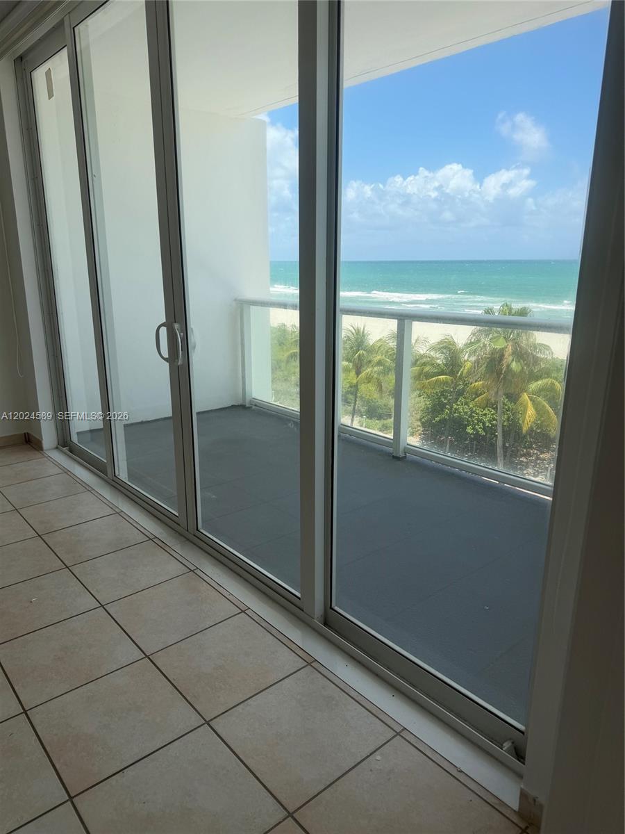 A tiled balcony overlooks the ocean through large sliding glass doors — 5601 COLLINS AV # 607, Miami Beach FL 33140, MIAMI BEACH, FL