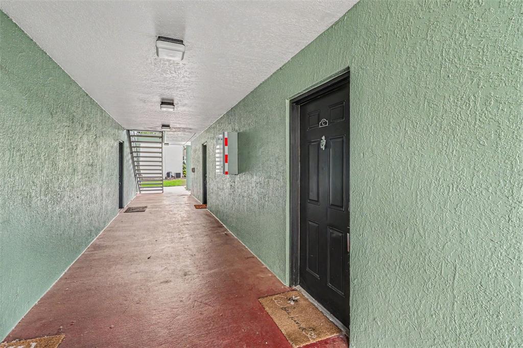 An outdoor apartment hallway with green textured walls, a black door, and metal stairs — 2031 DIXIE BELLE DRIVE UNIT 2031C, ORLANDO, FL