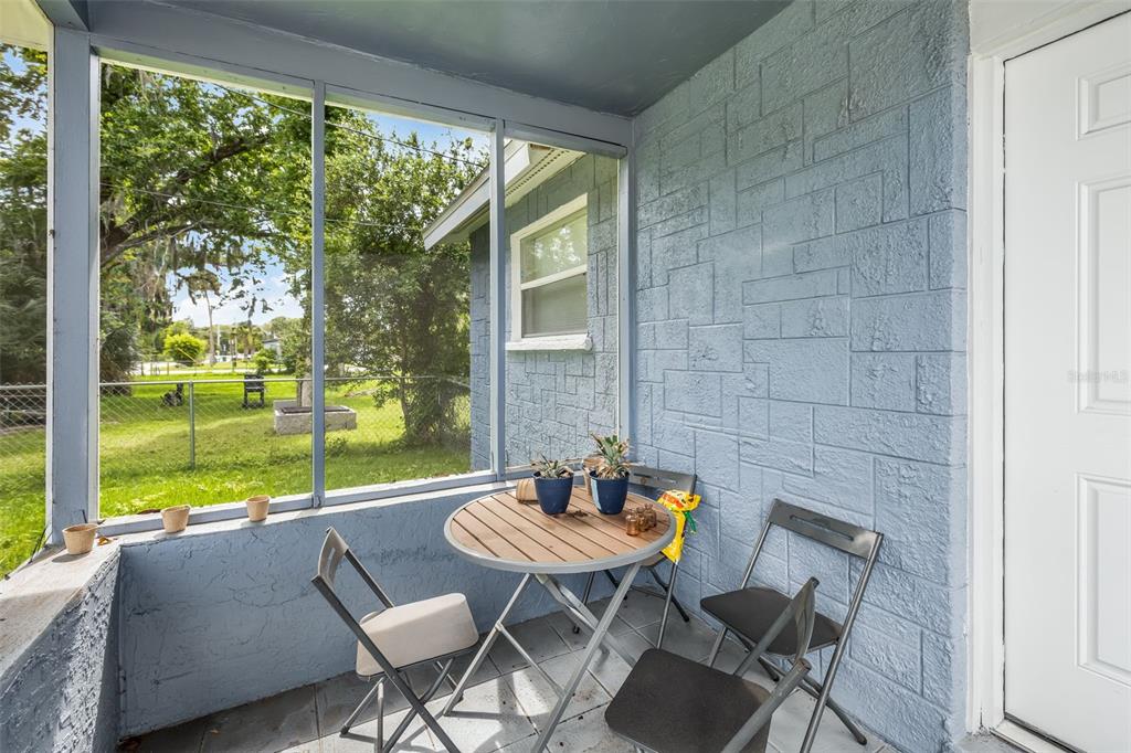 A screened-in porch features blue painted block walls, a small round table, and folding chairs — 906 MAGNOLIA AVENUE, DAYTONA BEACH, FL