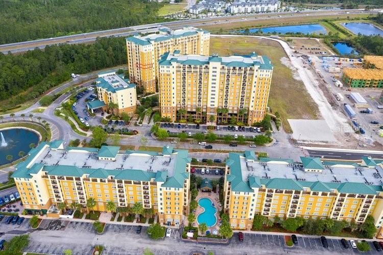An aerial view shows several large, multi-story yellow apartment buildings with green roofs and pools — 8101 RESORT VILLAGE DRIVE UNIT 31501, ORLANDO, FL