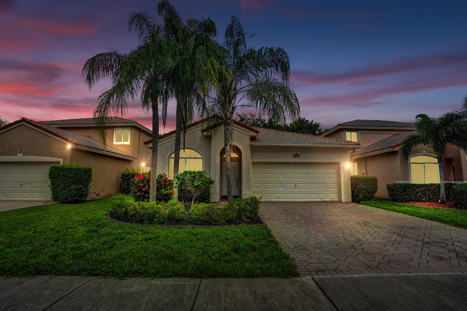 A beige suburban house with a paved driveway, palm trees, and a sunset sky — 3717 Pebblebrook Manor, Coconut Creek FL 33073, COCONUT CREEK, FL