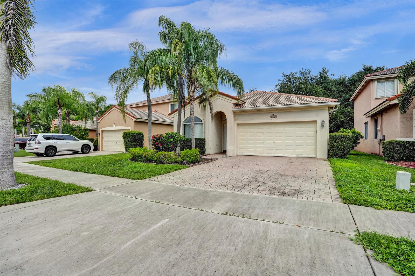 A single-story suburban house with a paved driveway, two-car garage, and palm trees — 3717 Pebblebrook Manor, Coconut Creek FL 33073, COCONUT CREEK, FL