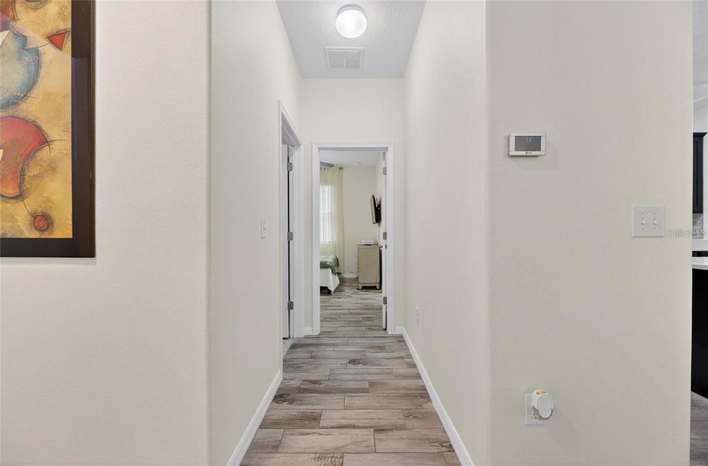 A hallway with wood-look tile flooring leads to a bedroom with a visible bed — 12113 ECHO BASIN COVE, RIVERVIEW, FL