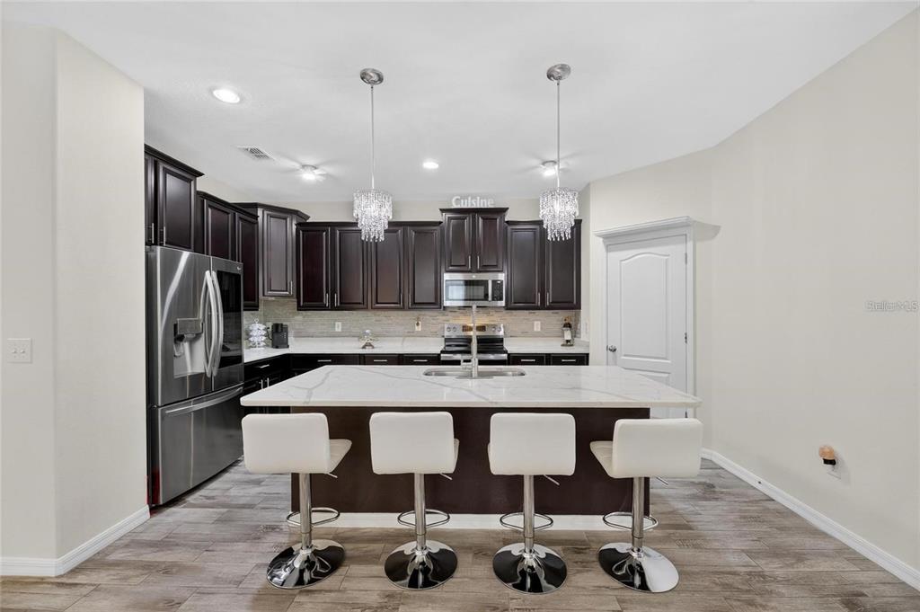 A kitchen features dark wood cabinets, a white marble island with four stools, and stainless appliances — 12113 ECHO BASIN COVE, RIVERVIEW, FL