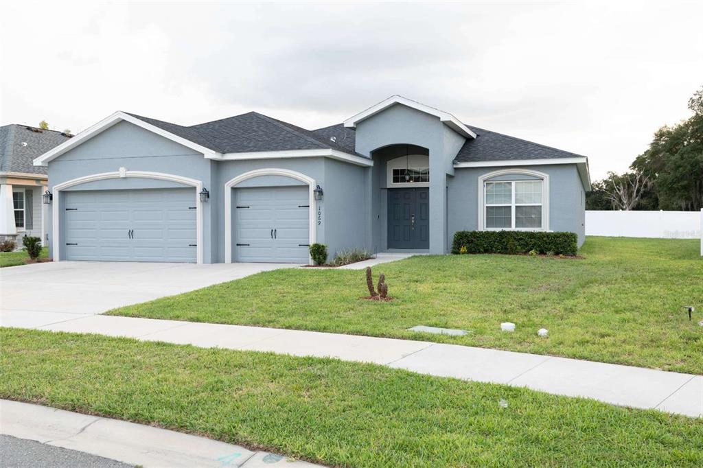 A single-story blue house with a three-car garage and a front entrance under an arch — 1069 MONTGOMERY LANE, POLK CITY, FL