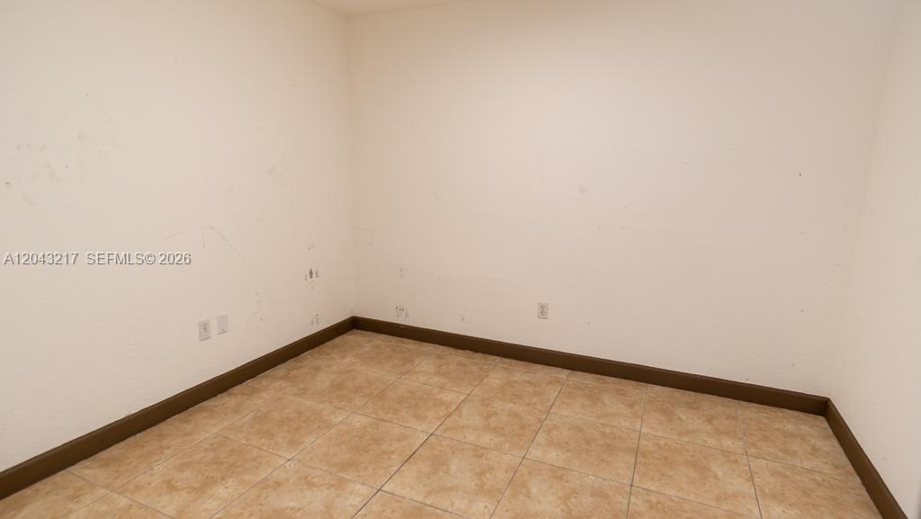 An empty room features beige tiled flooring, plain off-white walls, and dark brown baseboards — 8248 NW 22nd Ave, Miami FL 33147, MIAMI, FL