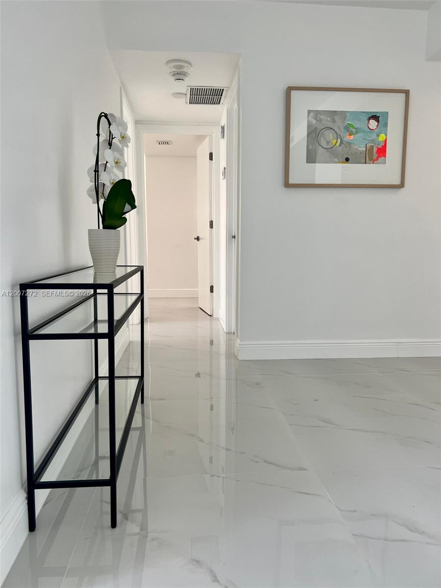 A hallway features white marble-look tile flooring, a black glass console table, and abstract art — 155 Ocean Lane Dr # 1011, Key Biscayne FL 33149, KEY BISCAYNE, FL