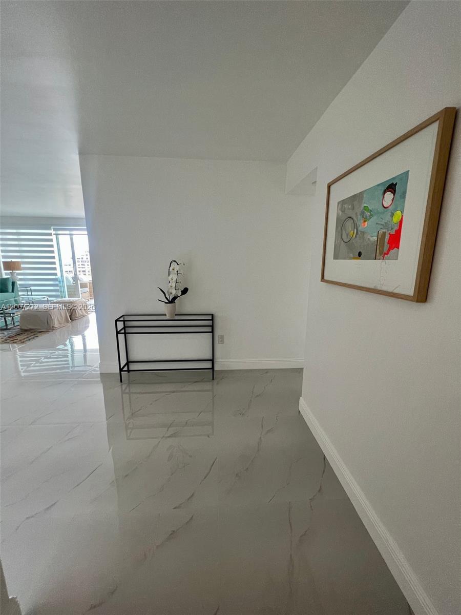 A white hallway with glossy tile flooring features a console table and framed wall art — 155 Ocean Lane Dr # 1011, Key Biscayne FL 33149, KEY BISCAYNE, FL