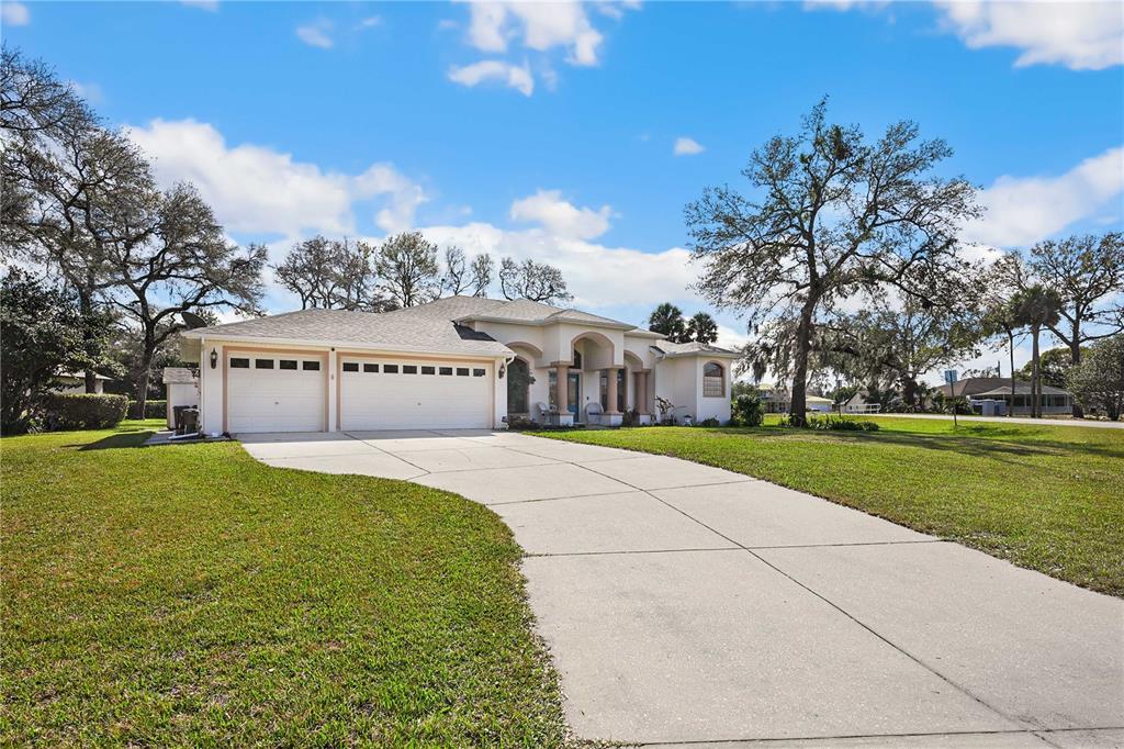 A single-story house with a three-car garage and a concrete driveway under a blue sky — 13855 RUDI LOOP, SPRING HILL, FL