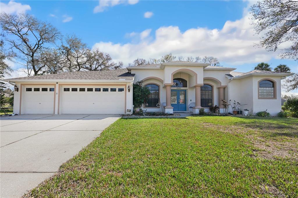 A single-story house with a three-car garage, arched windows, and a blue front door — 13855 RUDI LOOP, SPRING HILL, FL